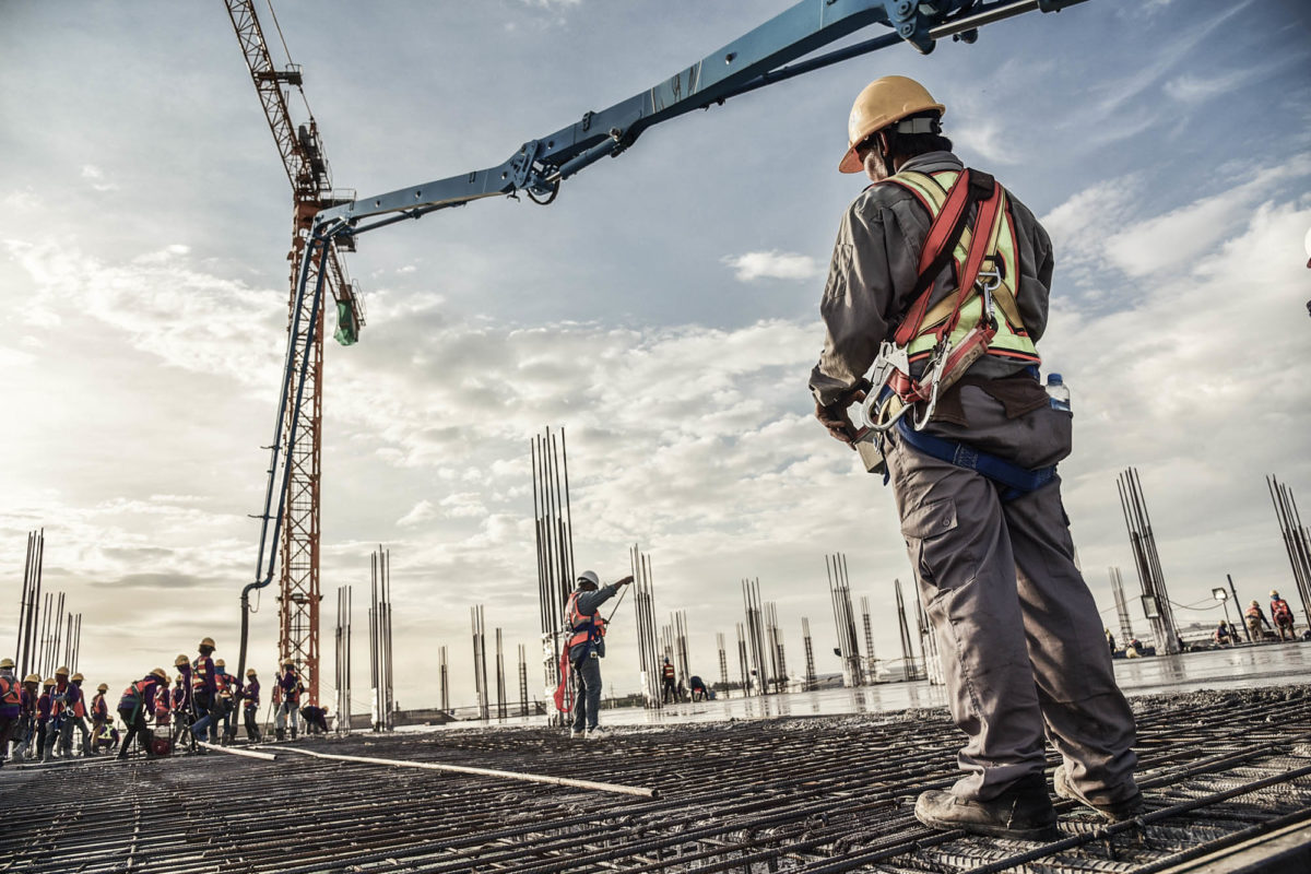 A construction worker control a pouring concrete pump on construction site and sunset background